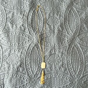 Long gold-color necklace with white pendant.